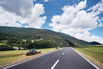 Landscape with asphalt road and a tractor in the field.