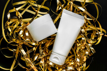 Empty white cosmetic tube and jar for face or hand cream on black background with christmas decor and golden streamers. Christmas and new year cosmetic gifts concept, unbranded cosmetics packaging.