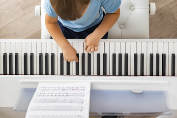 Cute baby boy playing white electrical forte piano pressing keys kid studying at musical school
