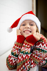 Girl in a knitted sweater and a santa claus hat. Holidays wellness concept.