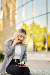 Fototapeta premium Businesswoman using a smartphone and digital tablet outdoors.