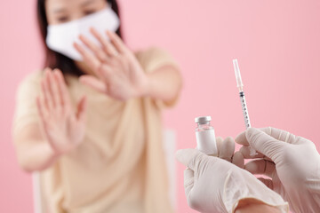 Doctor offering vial and syringe to scared young female patient in medical mask