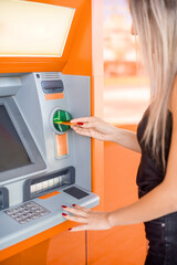A young blonde woman inserting a credit card into a bank ATM machine