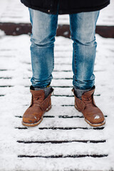 Man in blue jeans and old leather boots on snow. Old brown boots covered with snow.