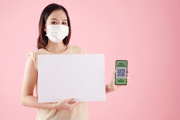 Young woman in protective mask holding white placard and smartphone with QR code indicating that she was vaccinated against covid-19