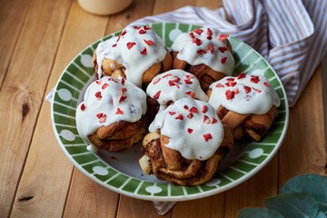 Cinnamon rolls with cream and freeze-dried strawberries, round yeast rolls. Side view, wooden background.