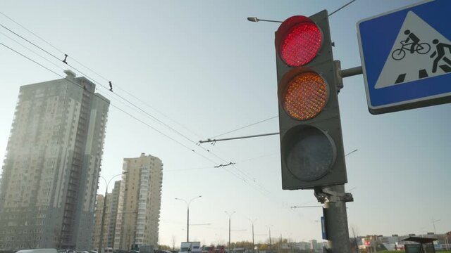 Urban traffic stoplight with LED lamps and changing signal colors at city street crossroads against buildings and blue sky