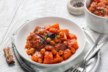 Pumpkin, lamb and chickpea stew with cinnamon sticks. Whie wood table.