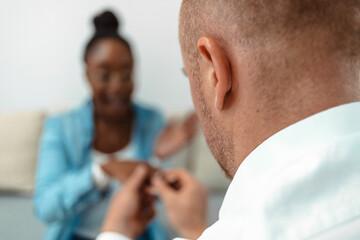 Shot of a young man proposing to his his girlfriend at home. Selective focus of young handsome bearded hipster man with engagement ring making proposal to his beautiful black woman at his home office.