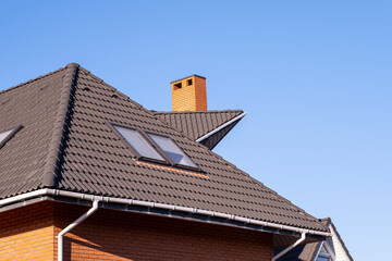 Roof with brown metal tiles and a dormer window. There are snow holders on the roof.