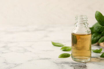 Glass bottle of basil essential oil and leaves on white marble table. Space for text