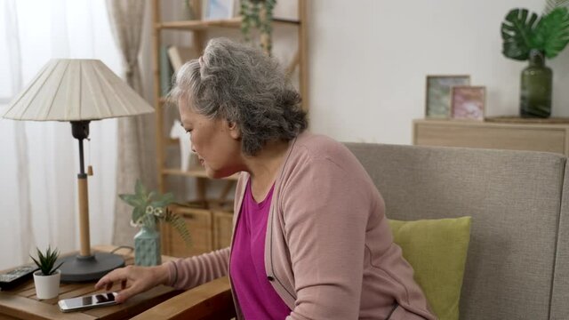korean grey haired grandma answering scam call from a stranger is feeling shocked at the bad news over the mobile phone in the living room at home