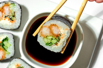 sushi roll with Tempura shrimp is kept in sticks and dipped in soy sauce. Close-up, selective focus