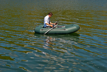 Naklejka premium A man in a white shirt on an inflatable boat. Businessman with laptop resting on the lake. The concept of remote work, leisure and freelance.