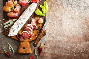 Board with tasty slices of salami and fresh grapes