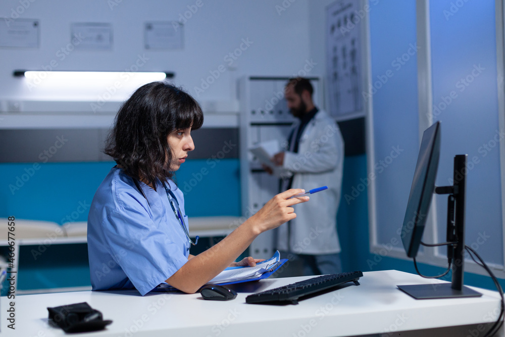 Poster nurse doing overtime work with computer and checkup files at office. medical assistant using informa