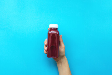 Female hands holding plastic bottles with juice or red smoothie on blue background. The concept of...