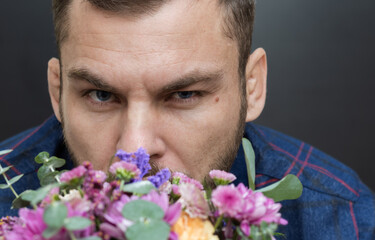 Charismatic man and colorful flowers. Adult 34 years old White Ethnicity man looks at the camera, colorful flowers in front of him.