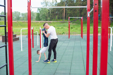 Caucasian man teaching son handstand at playground.