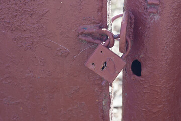 on the red iron gate hangs a closed iron overhang lock