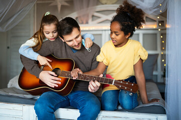 Smiling father with multiethnic children having fun and playing guitar at home