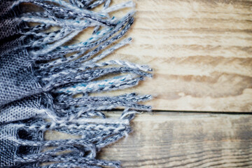 A warm plaid scarf with fringe lies on a light wooden background. The concept of comfort and warmth.