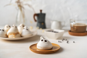 Meringues in a form of ghosts with cup of coffee, milk jar, chocolate drops and coffe pot on the light background