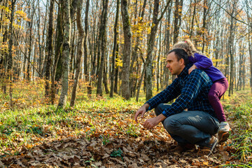 A child girl with her father in an autumn forest. A girl jumped on the back of a man in plaid coffee and jeans. The concept of a happy family.