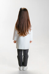 Back view. Cute beautiful little girl, child in image of doctor wearing white lab coat posing...