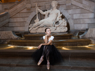 Pretty little girl sitting in a ballerina costume in front of a 1750 French statue of goddess of...