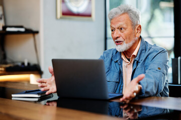 A senior student is sitting in the coffee shop and following online lectures on his laptop.