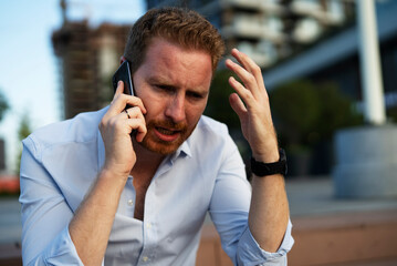 Businessman talking to the phone while sitting on the stairs. Angry upset man talking to the phone