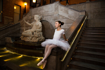 Pretty little girl sitting in a ballerina costume next to a 1750 French statue of goddess of the...