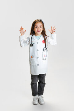 Preschool beautiful girl, child in image of doctor wearing white lab coat posing isolated on white studio background