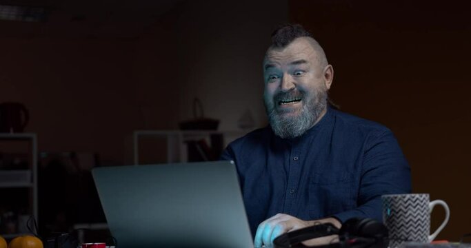 Bearded man laughs gloating while looking at the laptop screen. Sending an angry comment on social media
