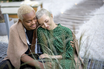 Latin man hugging his european girlfriend in their garden. Joyful multiracial couple enjoying time together. Concept of relationship. Modern domestic lifestyle. People covered in plaid