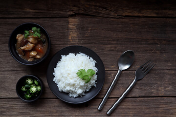 top view photo of jasmine rice is served on the wooden table with  chicken stew in gravy sauce or kao na kai in Thai language and green chilli for breakfast in the Thai traditional restaurant