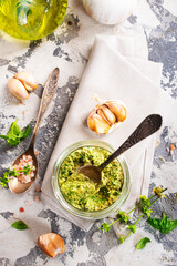 Homemade parsley pesto sauce and ingredients on dark cement background. Close up wiev of basil pesto in glass jar with ingredients.