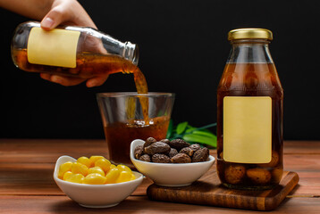 Chef pouring fruit extract drink from glass bottle into cup on dining table with food bowl of natural organic ginkgo and malva nut