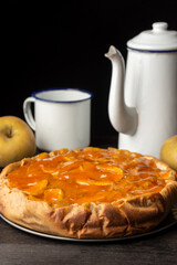 Top view of apple pie with cup and rustic coffee pot, selective focus, black background, vertical