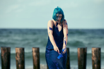Artistic blue-haired woman performance artist in dress smeared with blue gouache paints on her body