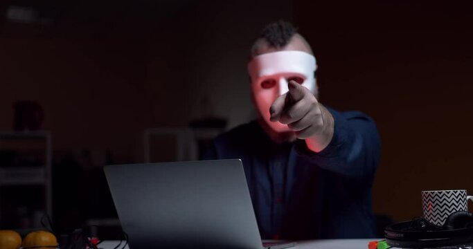 A man in a white mask incognito points a threatening finger at the camera. Computer cracker. Hacker.