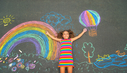 The child draws with chalk on the asphalt. Selective focus. - obrazy, fototapety, plakaty