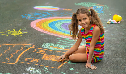 The child draws with chalk on the asphalt. Selective focus. - obrazy, fototapety, plakaty