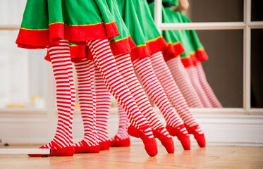 Legs of children dressed in costumes of Christmas elves practicing at a ballet bar in front of a...