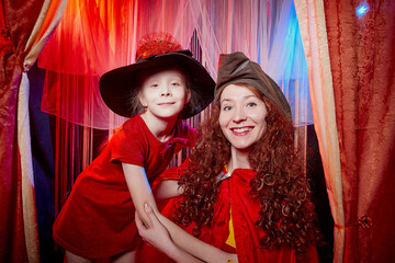 Family during a stylized theatrical circus photo shoot in a beautiful red location. Models mother and daughter posing on stage with curtain