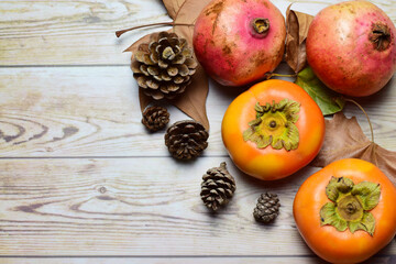 Top view, persimmon and pomegranate on rustic woods, decorated with dried natural leaves and pineapples.