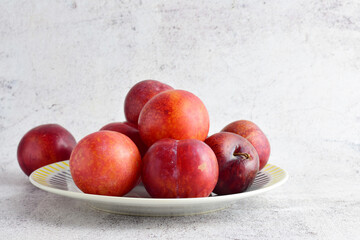 Close up, red plums on porcelain plate and stone background. 