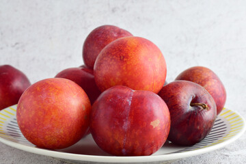 Close up, red plums on porcelain plate and stone background. 