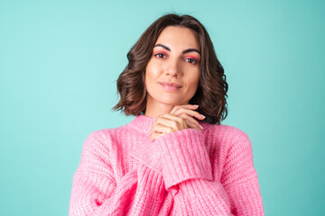Fototapeta premium Cozy portrait of a young woman in a pink knitted sweater and with bright makeup on a turquoise background